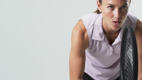 Focused-young-Caucasian-woman-prepares-for-a-tennis-match-on-a-white-background,-with-copy-space