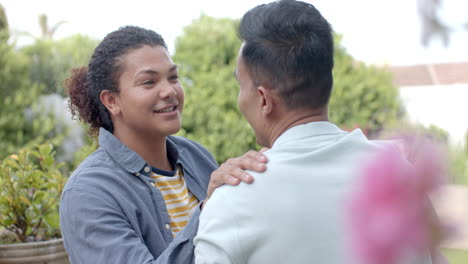 Happy-diverse-gay-male-couple-talking-and-smiling-sitting-in-sunny-garden,-slow-motion