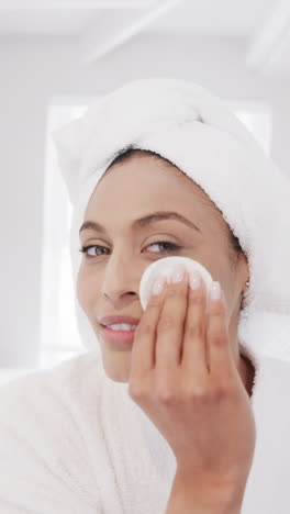 Vertical-video-of-portrait-of-happy-biracial-woman-applying-cleansing-face-in-bathroom,-slow-motion