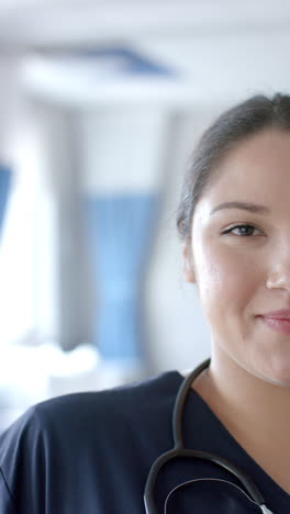 Vertical-video-half-portrait-of-biracial-female-doctor-smiling-in-hospital,-copy-space,-slow-motion