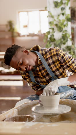 Happy-african-american-potter-using-potter's-wheel-and-smiling-in-pottery-studio,-slow-motion