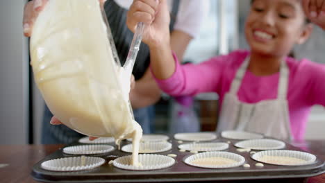 Happy-biracial-mother-and-daughter-pouring-cake-mix-into-cake-forms-in-kitchen,-slow-motion