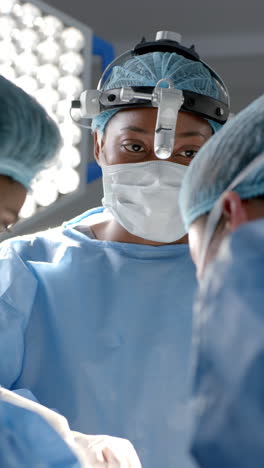 Vertical-video-of-diverse-female-surgeons-operating-on-patient-in-operating-theatre,-slow-motion