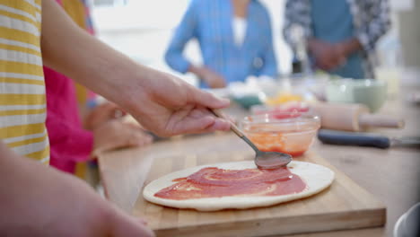 Diverse-group-of-teenage-friends-cooking-and-making-pizza-in-kitchen,-slow-motion