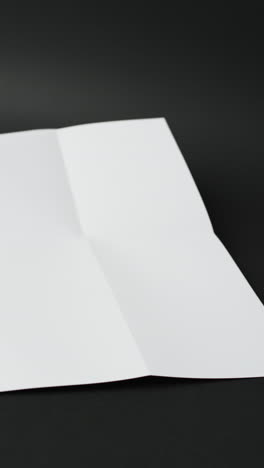 Vertical-video-of-piece-of-white-paper-with-creases-on-black-background