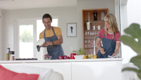 Happy-diverse-couple-cooking-and-throwing-waste-out-in-kitchen,-slow-motion