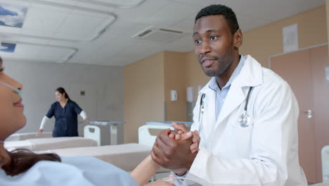 Médico-Varón-Diverso-Sosteniendo-La-Mano-De-Una-Paciente-Con-Oxímetro-En-La-Cama-De-Un-Hospital,-Cámara-Lenta