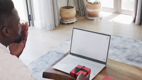 African-American-man-gestures-at-a-laptop-in-a-bright-home-office-on-a-video-call,-celebrating-a-spe