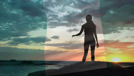 Animación-De-La-Bandera-De-Nigeria-Sobre-Una-Mujer-Caucásica-Feliz-Trepando-Rocas-Y-Viendo-La-Playa-Al-Atardecer