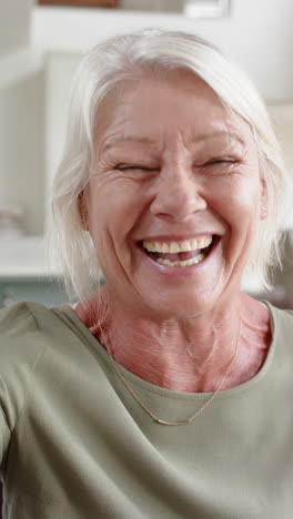 Glückliche,-Kaukasische-Seniorin-Mit-Videoanruf-Und-Küsschen-Im-Sonnigen-Zimmer,-Zeitlupe