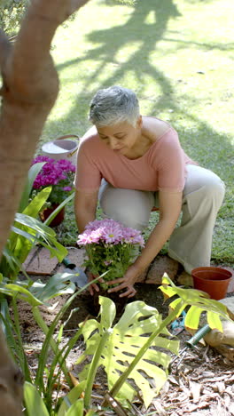 Video-Vertical-De-Una-Feliz-Mujer-Birracial-Mayor-Trabajando-En-El-Jardín,-Cámara-Lenta