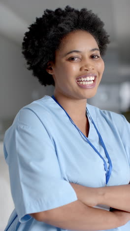 Vídeo-Vertical-Del-Retrato-De-Una-Feliz-Doctora-Afroamericana-En-El-Pasillo-Del-Hospital,-Cámara-Lenta