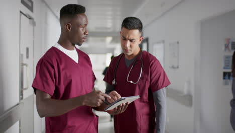 Diverse-male-doctors-discussing-work,-using-tablet-in-corridor-at-hospital,-slow-motion