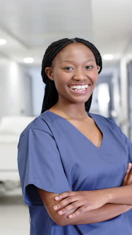 Vertical-video-of-portrait-of-happy-african-american-female-doctor-in-hospital,-slow-motion