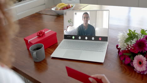 Caucasian-woman-holding-envelope-and-talking-with-biracial-man-on-laptop-screen