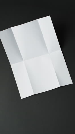 Vertical-video-of-piece-of-white-paper-with-creases-on-black-background