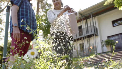 Feliz-Pareja-De-Ancianos-Birraciales-Regando-Plantas-En-Un-Jardín-Soleado