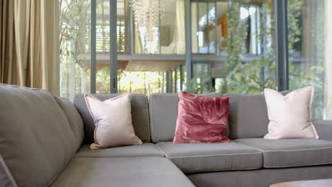 Brown-couch-with-pillows,-gold-curtains-and-huge-windows-in-sunny-living-room,-slow-motion