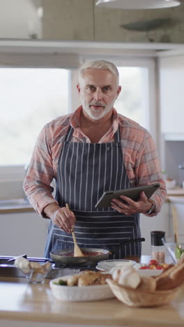 Vertical-video-of-portrait-of-happy-senior-caucasian-man-preparing-dinner-in-kitchen,-slow-motion