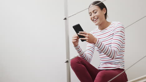 Mujer-Birracial-Feliz-Sentada-En-Las-Escaleras-Usando-Un-Teléfono-Inteligente,-Cámara-Lenta