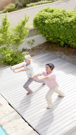 Dos-Mujeres-Mayores-Felices-Y-Diversas-Practicando-Yoga-En-Un-Jardín-Soleado,-Cámara-Lenta