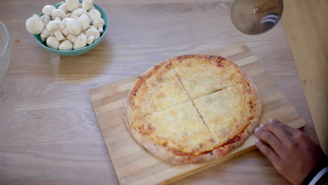 Happy-african-american-male-teenager-cutting-pizza-on-table-in-kitchen,-slow-motion