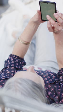 Vertical-video-of-senior-caucasian-woman-using-smartphone-with-copy-space-in-hammock,-slow-motion