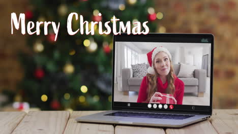 Animation-of-merry-christmas-text-over-caucasian-woman-on-laptop-screen-and-christmas-decorations