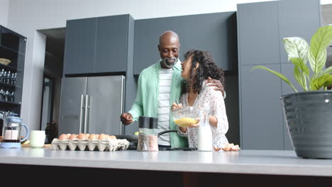 Happy-biracial-couple-cooking-and-preparing-omelet-on-pan-in-kitchen,-slow-motion