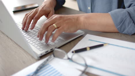 Midsection-of-senior-biracial-man-using-laptop-sitting-at-table,-working-from-home,-slow-motion