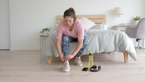 Plus-size-biracial-woman-sitting-on-bed-preparing-for-exercising,-copy-space,-slow-motion