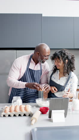 Vertical-video-of-happy-diverse-mature-couple-using-tablet-baking-at-home,-copy-space,-slow-motion