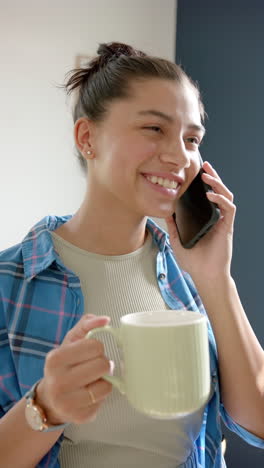 Video-Vertical-De-Una-Adolescente-Birracial-Sonriente-Con-Té-Hablando-En-Un-Teléfono-Inteligente,-Cámara-Lenta