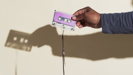 Video-of-african-american-man's-hand-holding-retro-tape-with-copy-space-on-yellow-background