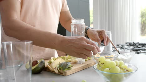 Midsection-of-senior-biracial-man-preparing-healthy-smoothie-in-kitchen-at-home,-slow-motion