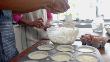 Midsection-of-biracial-mother-and-daughter-baking,-preparing-cake-mix-in-kitchen,-slow-motion