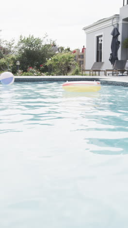 Vertical-video-senior-african-american-female-friends-sitting-by-sunny-pool,-copy-space,-slow-motion