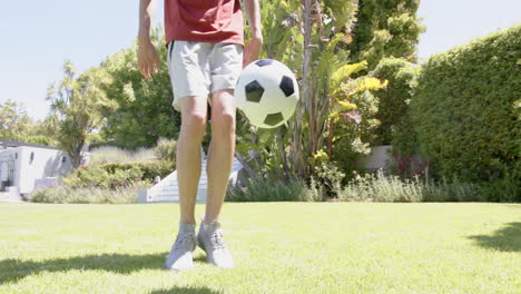 Sección-Baja-De-Un-Hombre-Birracial-Practicando-Habilidades-Con-El-Fútbol-En-Un-Jardín-Soleado,-Espacio-Para-Copiar,-Cámara-Lenta