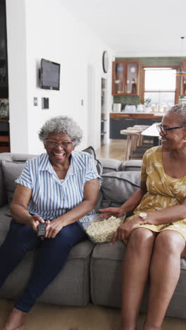 Vertical-video-of-senior-african-american-female-friends-watching-tv,-copy-space,-slow-motion