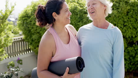 Dos-Mujeres-Mayores-Felices-Y-Diversas-Con-Colchonetas-De-Ejercicio,-Abrazándose-Y-Sonriendo-En-El-Jardín,-Cámara-Lenta