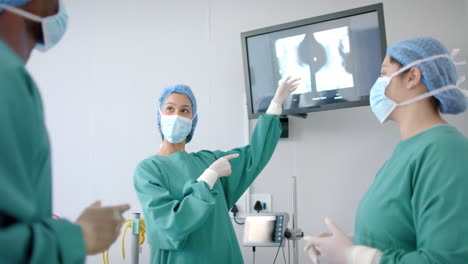 Diverse-female-and-male-surgeons-in-masks-discussing-x-ray-in-operating-theatre,-slow-motion