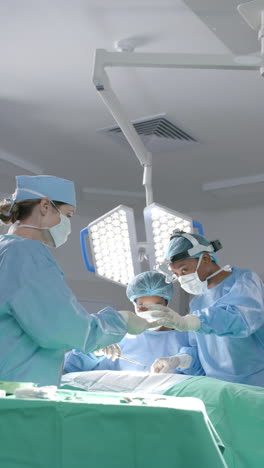 Vertical-video-of-diverse-female-surgeons-operating-on-patient-in-operating-theatre,-slow-motion