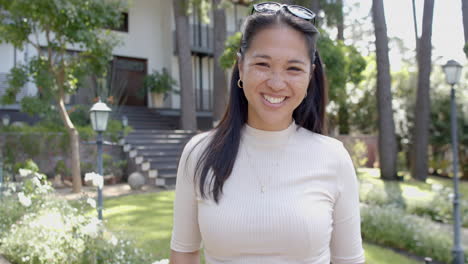 Happy-asian-woman-with-sunglasses-standing-and-smiling-in-sunny-garden,-slow-motion