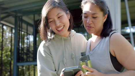 Felices-Amigas-Asiáticas-Con-Botella-De-Agua-Y-Teléfono-Inteligente-Riéndose-En-La-Terraza,-Cámara-Lenta