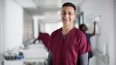 Portrait-of-happy-biracial-male-doctor-wearing-scrubs-in-hospital,-copy-space,-slow-motion