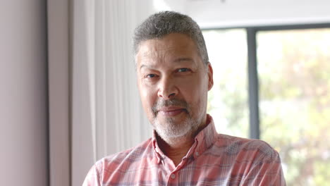 Portrait-of-happy-senior-biracial-man-smiling-in-sunny-room-at-home,-slow-motion