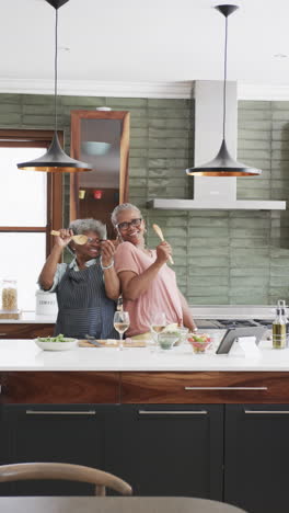 Video-Vertical-De-Amigas-Afroamericanas-Mayores-Cantando-En-La-Cocina,-Espacio-Para-Copiar,-Cámara-Lenta