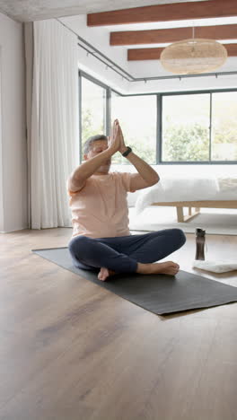 Vertical-video-of-senior-biracial-man-practicing-yoga-meditation-at-home,-vertical