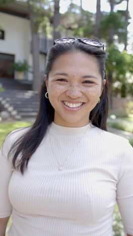 Happy-asian-woman-with-sunglasses-standing-and-smiling-in-sunny-garden,-slow-motion