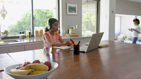 Biracial-Mädchen-Mit-Kopfhörern-Beim-Grundschulunterricht-Am-Laptop,-Kopierraum,-Zeitlupe